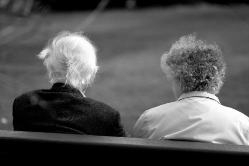 Two older women sitting on a park bench.